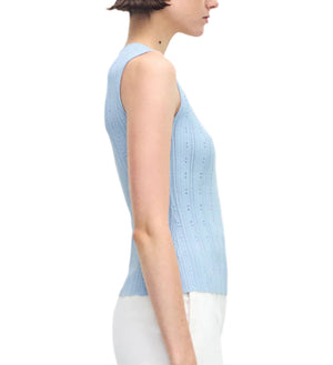 A woman in profile wears the Brynn Top Compact Jacquard by Adam Lippes, a light blue, rib-stitch sleeveless top with a fitted bodice, paired with white pants against a plain background.