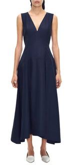 A woman wears the Adam Lippes Harlow Dress, a sleeveless V-neck in rich navy. Its ankle-length, flared cotton poplin skirt pairs perfectly with her white shoes, offering a chic and timeless look.