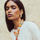 Woman with long black hair wears a white top, colorful handcrafted beaded necklace, and Lizzie Fortunato Zellige Hoops, standing against a textured beige wall.