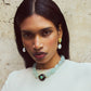 A woman with long dark hair, pearl earrings, and a white top wears the Lizzie Fortunato Andalusia Collar—a blue beaded necklace with turquoise accents and a black pendant—against a textured beige wall.