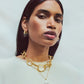 A woman with straight dark hair wears gold hoop earrings and the Lizzie Fortunato Oasis Necklace, a delicate gold chain with a pearl pendant, against a plain light background.