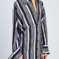 A person wears the Amira Dress by Proenza Schouler, a long-sleeved, button-down shirtdress with vertical black, white, and blue stripes in luxe Printed Silk Habotai, standing against a plain background.