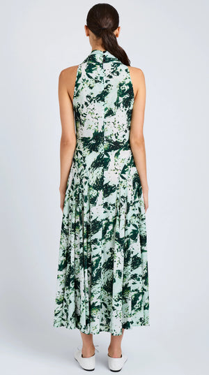 A woman faces away in the Proenza Schouler Adelide Dress—a sleeveless, ankle-length green and white printed silk viscose fit-and-flare dress—paired with white shoes.
