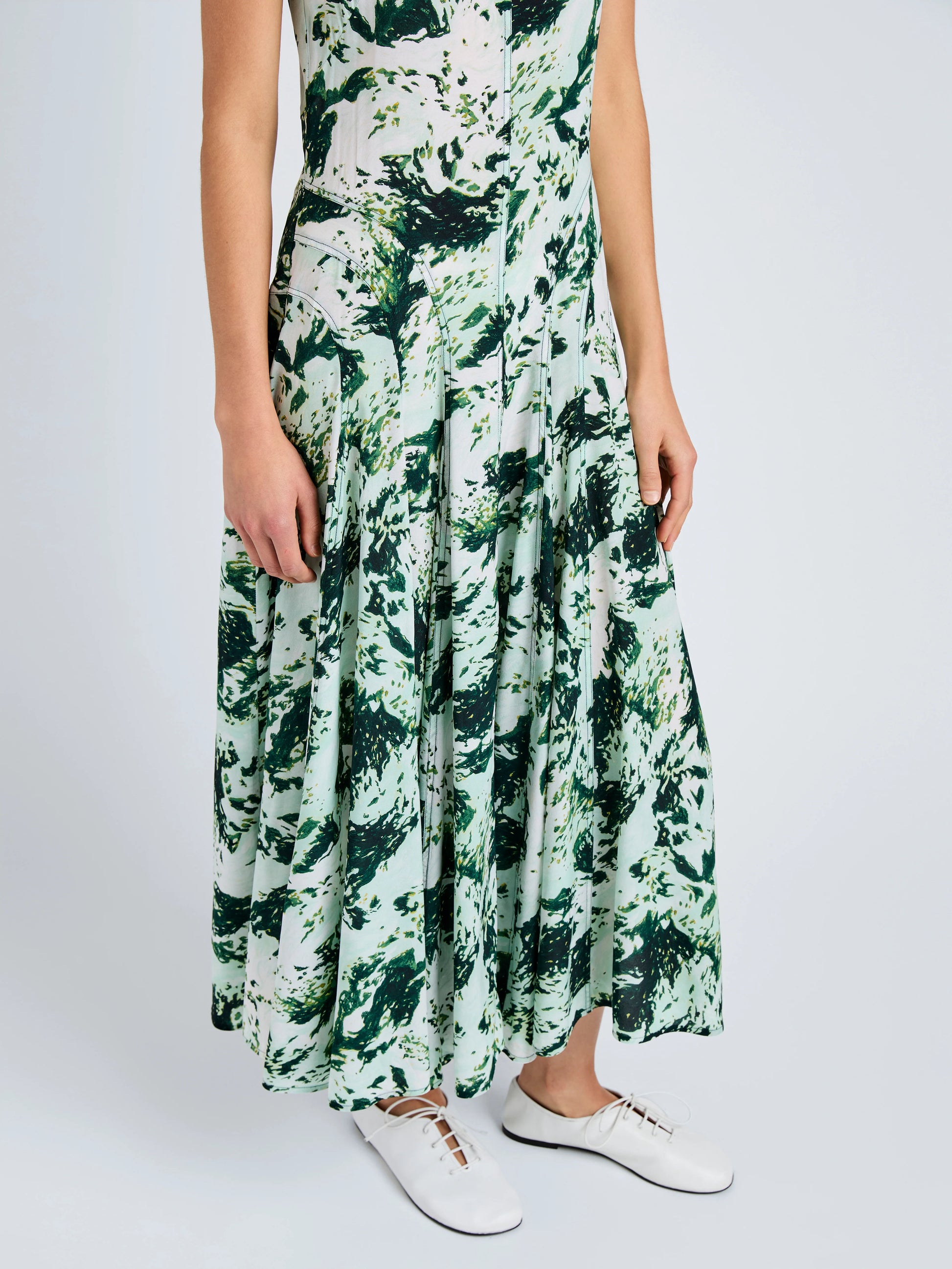 A person wears the Proenza Schouler Adelide Dress—a sleeveless, green and white silk-viscose dress with a fit-and-flare silhouette—and white lace-up shoes, standing against a plain background.