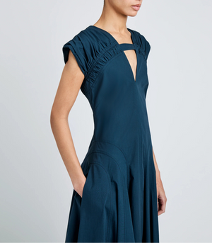 A person is shown from the side wearing the Manoela Dress by Proenza Schouler in dark teal Eco Light Compact Poplin, featuring ruched short sleeves and a V-shaped neckline.