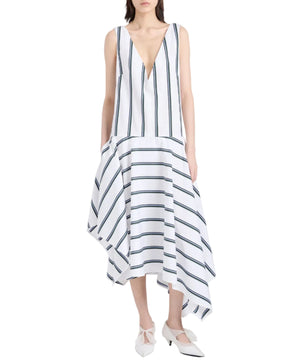 Woman wears the Beatriz Dress by Proenza Schouler, a sleeveless V-neck style in Cotton Silk Shirting with black stripes, an asymmetrical scarf hem, and paired with white heels.