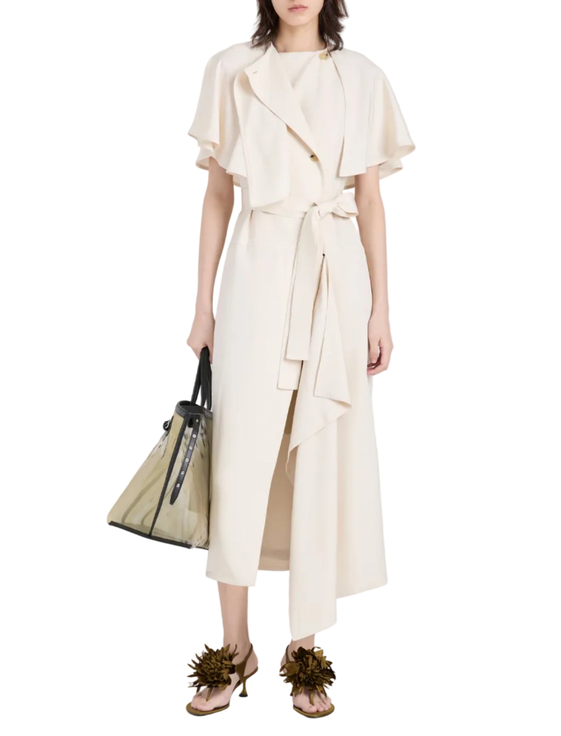 A person wears the Proenza Schouler Isolde Dress, a cream trench-inspired wrap dress with a short cape, paired with a transparent handbag and embellished heeled sandals.