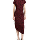 A woman wears the Proenza Schouler Ren Printed Dot Dress, a short-sleeve burgundy midi dress with black polka dots, side draping, and an asymmetrical hem, paired with black heeled shoes.
