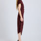 A person stands in profile against a plain light background wearing the Proenza Schouler Ren Printed Dot Dress—maroon with black polka dots, crafted from stretch viscose—paired with black heels.
