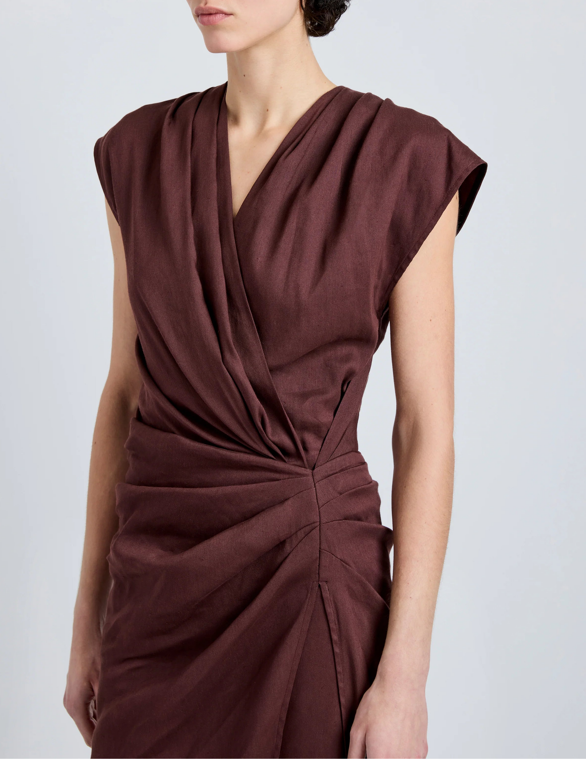 A person wearing the Proenza Schouler Bettina Dress, a sleeveless deep burgundy wrap made from Eco Stretch Viscose Linen with gathered waist detail, photographed from shoulders to mid-thigh.