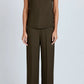 A model wears the Proenza Schouler Defni Top, a sleeveless olive brown piece with a draped high neckline in Eco Hammered Viscose, paired with matching wide-leg trousers against a plain light background.