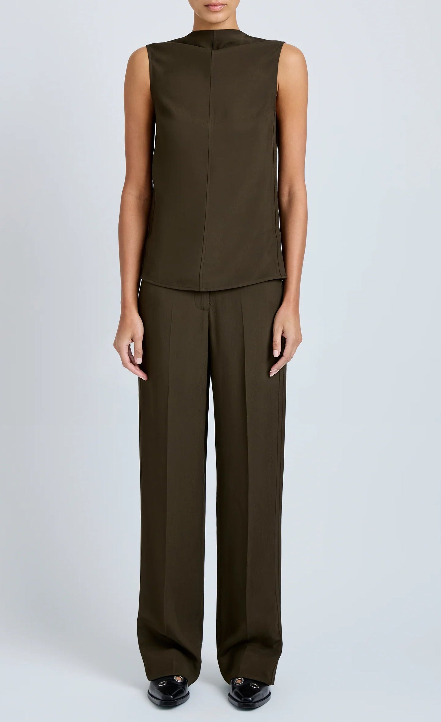 A model wears the Proenza Schouler Defni Top, a sleeveless olive brown piece with a draped high neckline in Eco Hammered Viscose, paired with matching wide-leg trousers against a plain light background.