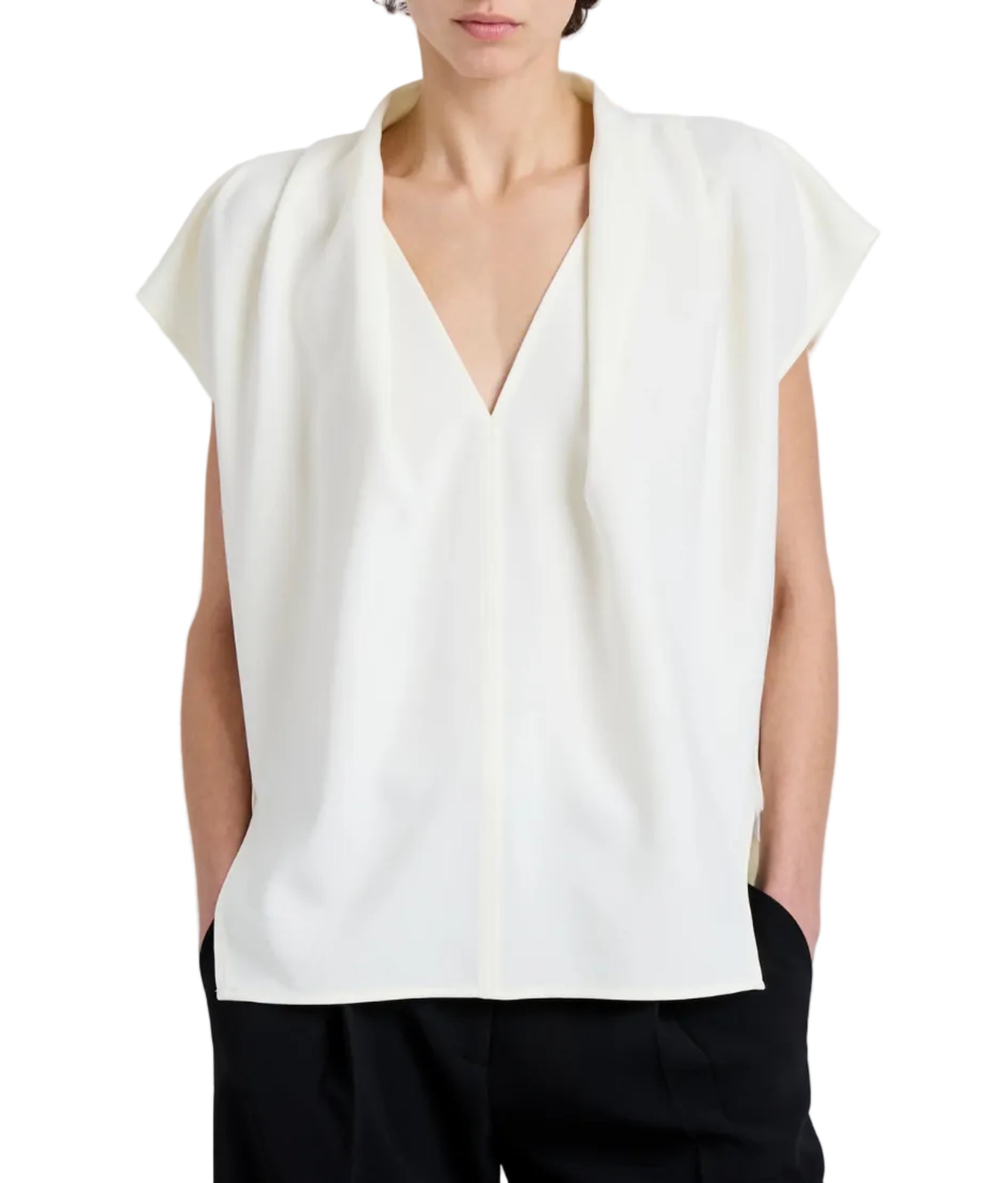 A person is wearing the Proenza Schouler Ranli Top, a loose-fitting, sleeveless white V-neck blouse with a draped collar, paired with black pants and hands in pockets.