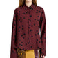 A woman wears the Proenza Schouler Paz Printed Dot Shirt, a maroon stretch viscose top with black polka dots, paired with a snakeskin-patterned skirt featuring yellow and brown panels.