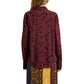 A person is shown from the back wearing the Paz Printed Dot Shirt by Proenza Schouler, a maroon stretch viscose top with black polka dots, paired with a skirt featuring vertical yellow, brown, and black panels.