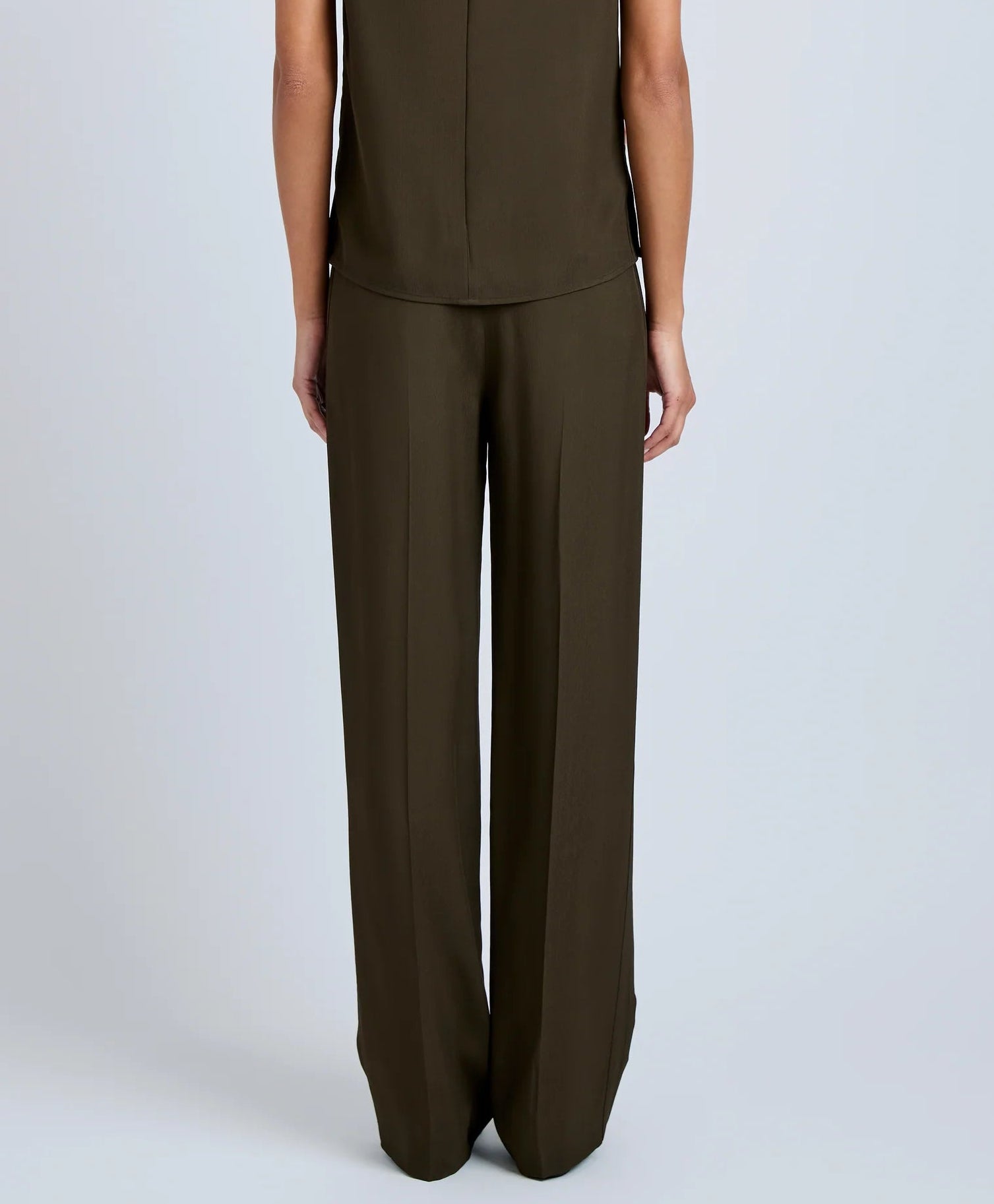 A person faces away from the camera, wearing the Proenza Schouler Lien Pant in high-waist olive green with a matching sleeveless Eco Hammered Viscose top, set against a plain light background.