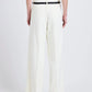A person wearing the Proenza Schouler Halima Pant in white high-waisted matte double crepe, paired with a white sleeveless top, black braided belt, and heeled sandals, stands facing away against a plain background.