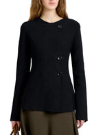 A woman wearing the Proenza Schouler Sukki Jacket in black with long sleeves and an asymmetrical button-up design, paired with an olive green skirt and holding a brown bag.