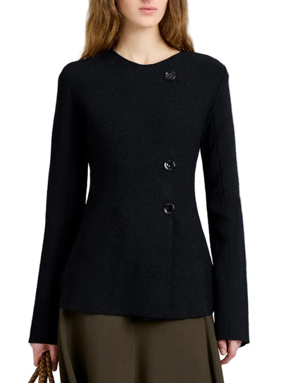 A woman wearing the Proenza Schouler Sukki Jacket in black with long sleeves and an asymmetrical button-up design, paired with an olive green skirt and holding a brown bag.
