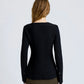 A woman with long brown hair is seen from behind wearing the Sukki Jacket by Proenza Schouler in black, paired with an olive green skirt against a plain light background.