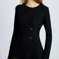 A woman wears the Sukki Jacket by Proenza Schouler, a tailored black jacket with an asymmetric front and three large black buttons, paired with olive green pants.