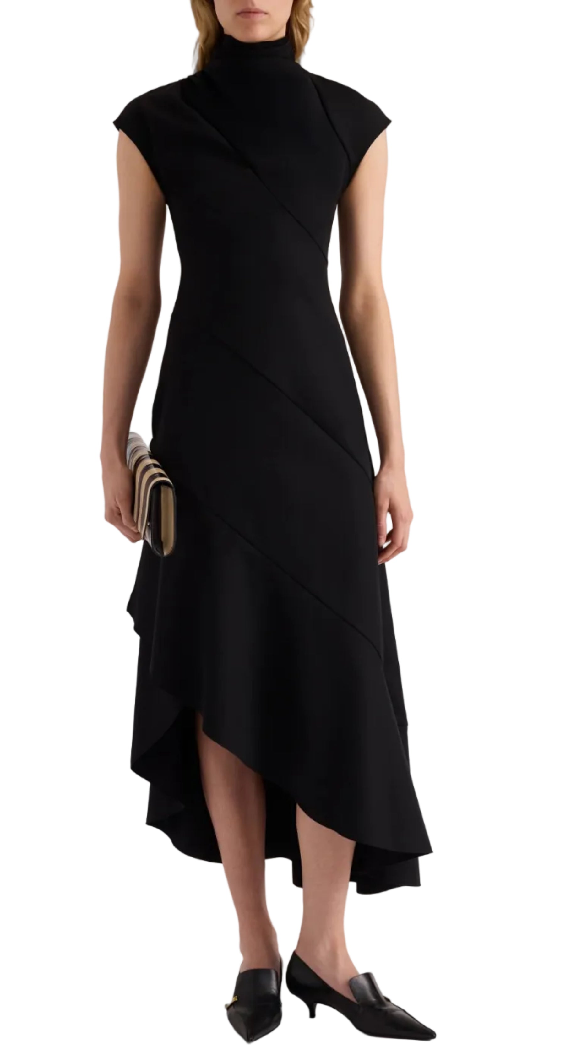 A person wearing the Elodine Tropical Wool Dress by Proenza Schouler—a sleeveless, black asymmetrical midi dress with a high neck crafted from luxurious tropical wool—paired with a striped clutch and black pointed-toe kitten heel shoes.
