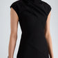 A woman wearing the Proenza Schouler Elodine Tropical Wool Dress—a black, short-sleeve, high-neck style with a transitional silhouette—holds a cylindrical clutch with black and beige stripes.