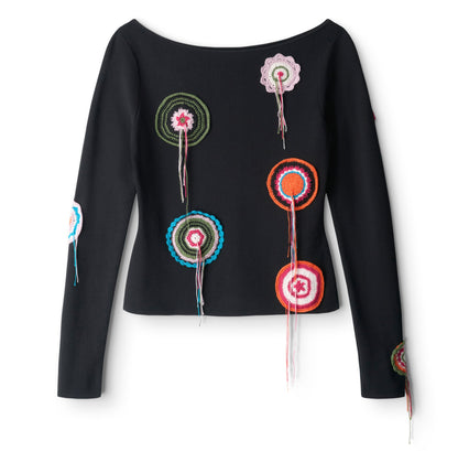 The Rimini Top by Staud is a black slim long-sleeve top with a boat neckline, accented with colorful crocheted circular doily appliqué patches and hanging yarn strands on the front and sleeves.
