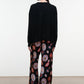 A person stands with their back to the camera, wearing a black sweater paired with Staud’s Stroll Silk Pant—a wide-leg silhouette adorned with a colorful circular pattern that drapes effortlessly against a plain background.