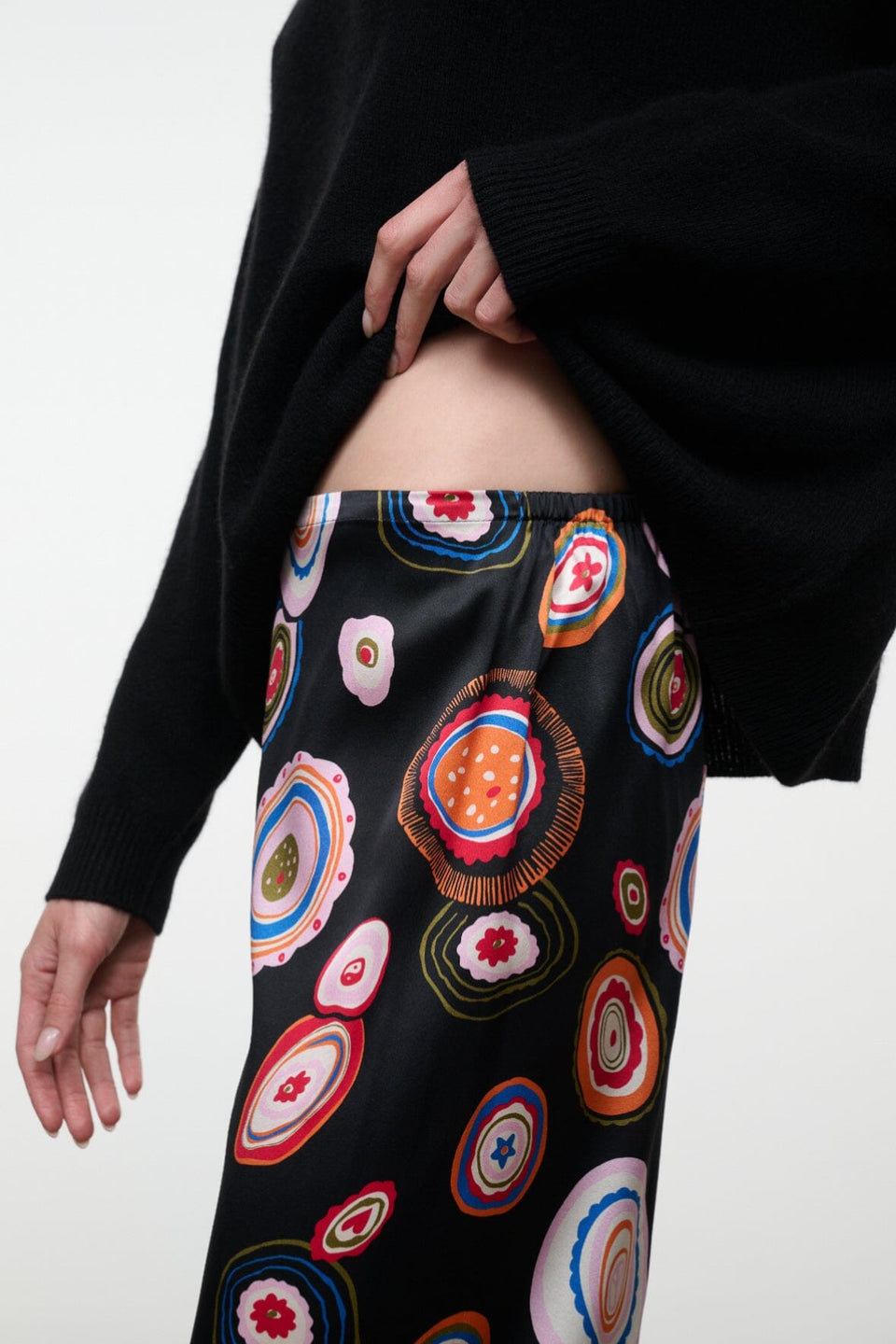 Person wearing Staud’s Stroll Silk Pant, paired with a black sweater, showing part of their midriff against a plain background—the look captures an effortless drape that adds movement and ease to the ensemble.