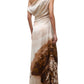 A person wearing the Staud Phare Silk Maxi Dress, featuring a one-shoulder neckline and floor-length silhouette with a printed landscape scene, stands in profile facing away from the camera.