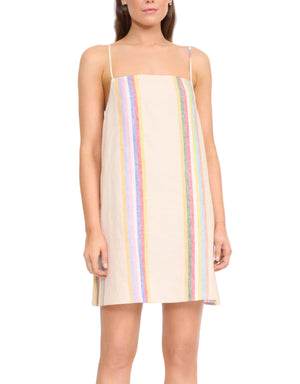 A woman wears the Laura Linen Mini Dress by Staud, a mini dress with spaghetti straps and vertical multicolored stripes on a light background.