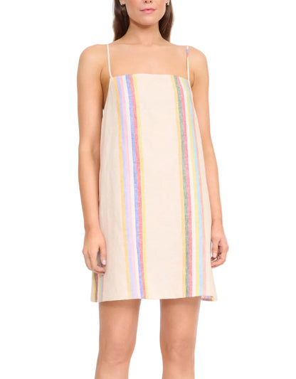 A woman wears the Laura Linen Mini Dress by Staud, a mini dress with spaghetti straps and vertical multicolored stripes on a light background.