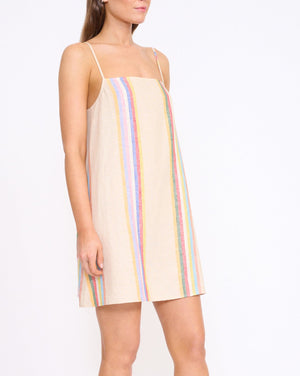 A woman models the Staud Laura Linen Mini Dress—sleeveless, beige, with summer stripe accents—against a plain white background.
