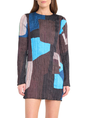 A woman wears the Staud Kona Dress, a long-sleeve textured mini featuring an abstract geometric pattern in blue, black, brown, and beige.