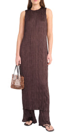 A woman in the Staud Mizu Dress—a sleeveless, ankle-length brown textured dress—paired with matching wide-leg pants, black sandals, and a brown woven handbag.