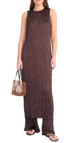 A woman in the Staud Mizu Dress—a sleeveless, ankle-length brown textured dress—paired with matching wide-leg pants, black sandals, and a brown woven handbag.