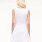 A person with long, light blonde hair is shown from the back, wearing the Staud Gwen Mini Dress—a sleeveless white poplin style with structured pleats—against a plain, light background.