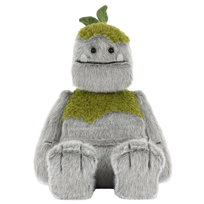 Rockleton by Jellycat is a gray, furry plush monster with two small white tusks, green patches on its head and chest, and fabric leaves on top.