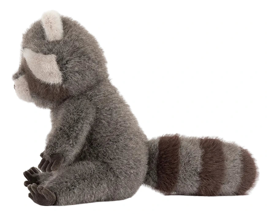 The Jellycat Trixiwoo Raccoon plush toy is pictured in profile, sitting upright with a striped tail and detailed fur, showcasing its charming and lifelike design.