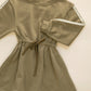 The Rylee & Cru Girls’ Tate Dress in olive green, featuring long sleeves with delicate lace trim, an adjustable drawstring, and a gathered waist, is shown laid flat on a light background.