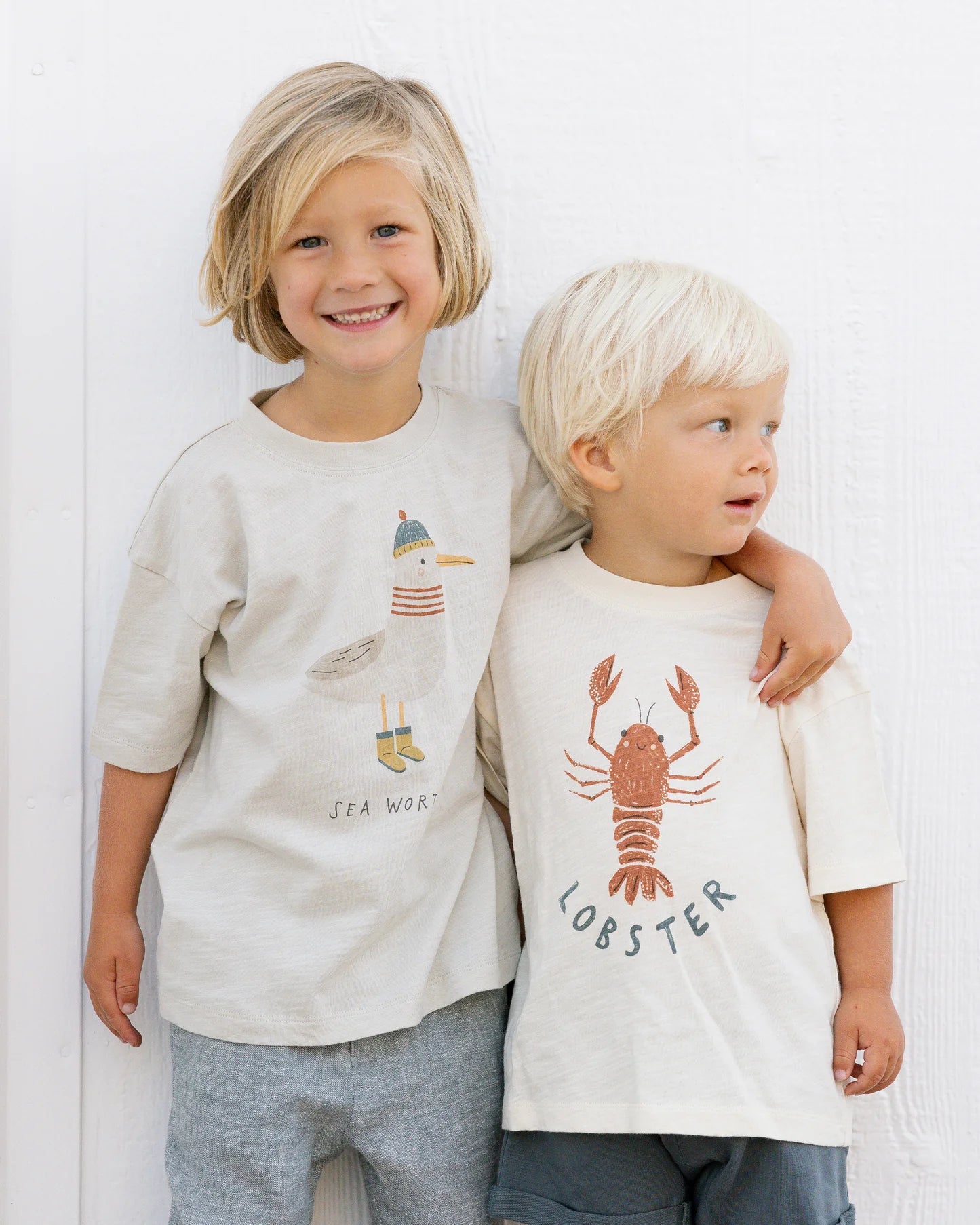Two children stand side by side against a white wall, both wearing Rylee & Cru Baby Boys' & Boys' Relaxed Tee—crafted from soft cotton jersey and available in baby sizes.