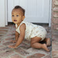 A baby wearing the Rylee & Cru Baby Boys' Bubble Onesie with nautical print crawls on a brick floor near a white door and brick wall.