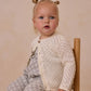 A young blonde girl with pigtails sits on a wooden chair, wearing the Rylee & Cru Baby Girls' Crochet Cardigan and matching pants with a delicate light pattern, looking slightly off camera.