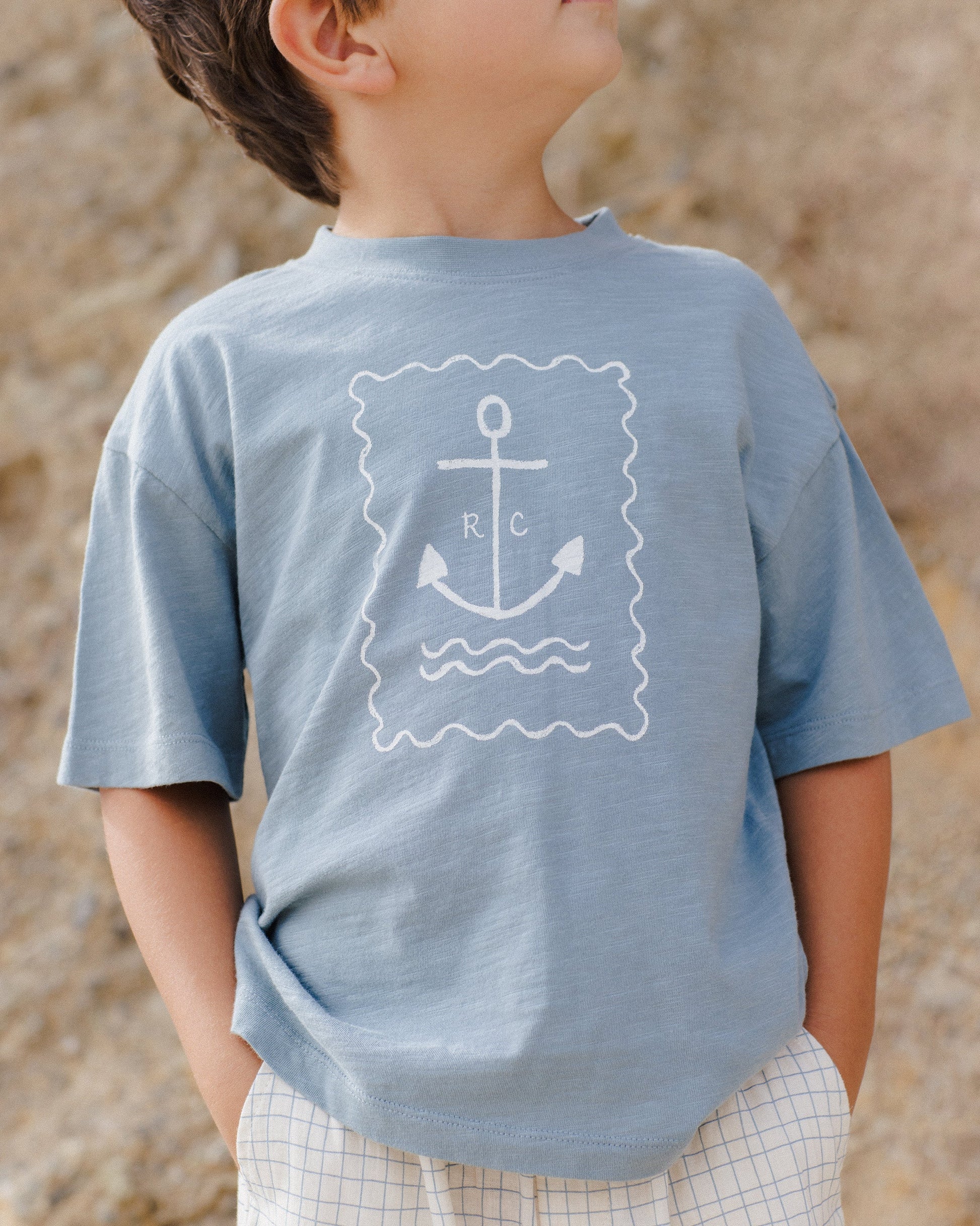 A child wears the Rylee & Cru Baby Boys' and Boys' Relaxed Tee, crafted from soft cotton jersey with an anchor spot and wave print, while standing outdoors by rocky terrain.