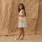 Young girl in the Rylee & Cru Girls' Crochet Tank Mini Dress, holding a straw purse and standing on a mat with a crumpled paper backdrop.