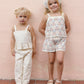 Two young children stand side by side against a pale pink wall, both wearing the Rylee & Cru Girls' Lili Knit Set, featuring light-colored crochet tanks with delicate ruffled trim, looking at the camera.