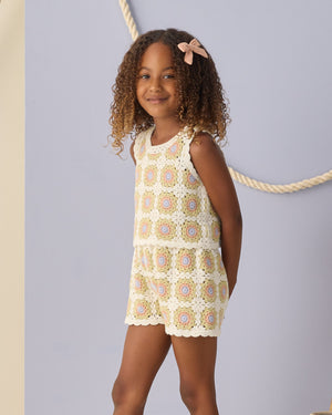 A young girl with curly hair wears the Rylee & Cru Girls' Crochet Tank Set, featuring ruffled trim, standing before a light blue wall with a rope decoration.