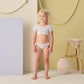 A young girl stands indoors wearing the Rylee & Cru Girls' Cropped Rashguard Set, surrounded by neutral and pastel decor featuring a rope, stool, basket, and vase in the background.