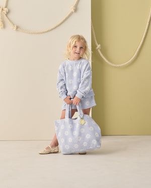 A young girl holds the Rylee & Cru Terry Beach Bag, standing indoors against a beige and olive green wall with rope decor.